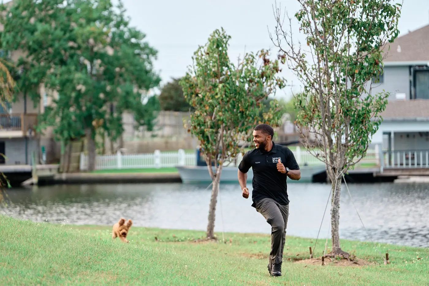 Walter Bell running across the grass beside the water while a puppy chases him